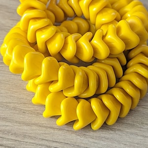 May include: A close-up of a strand of yellow glass beads. The beads are shaped like small, pointed leaves and are arranged in a spiral pattern.