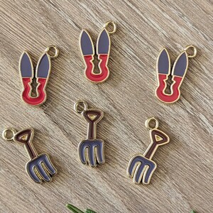 May include: Six gold charms with enamel details. Two charms are shaped like a pair of scissors with red and purple enamel. Two charms are shaped like a garden fork with purple enamel. Two charms are shaped like a garden rake with purple enamel.