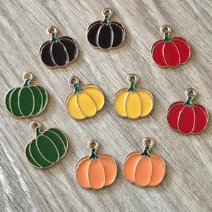 May include: A collection of ten metal pumpkin charms featuring colorful enamel fill. The set includes two dark purple, two red, two green, two yellow, and two orange pumpkins, each with a small metal loop at the top for attachment purposes.