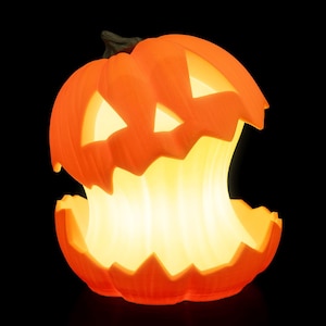 Könnte beinhalten: Eine beleuchtete orangefarbene Halloween-Laterne mit einem geschnitzten Gesicht und einem großen, offenen Mund. Das Innere leuchtet mit einem warmen, gelben Licht und schafft eine festliche Halloween-Dekoration. Der Kürbis steht vor einem schwarzen Hintergrund.