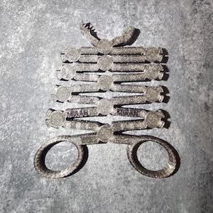 May include: A silver metal scissor-like tool with multiple rings stacked on top of each other. The rings are connected by a metal bar that forms the handles of the tool.