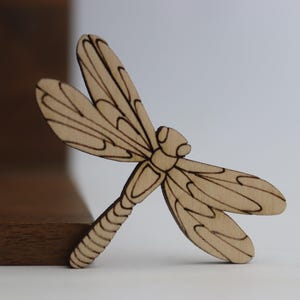Puede incluir: Un recorte de libélula de madera con detalles intrincados, perfecto para manualidades o decoración del hogar.