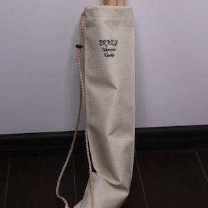 K&ouml;nnte beinhalten: Beige Canvas-Tasche mit Kordelzug, die zwei zylindrische Holzobjekte enth&auml;lt. Auf der Tasche befindet sich ein gr&uuml;nes Logo mit dem Text "ERUL Ukraine Kharkiv". Ein beiges Seil ist befestigt.