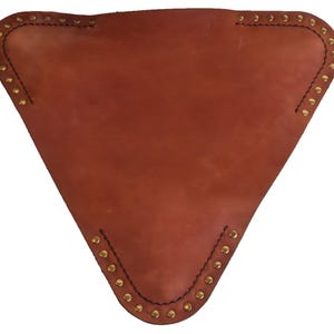 K&ouml;nnte beinhalten: Ein braunes, dreieckiges Objekt aus Leder mit Messingnieten an den Kanten. Das Leder hat eine nat&uuml;rliche Maserung und ein leicht abgenutztes Aussehen. Die Kanten sind mit schwarzem Faden gen&auml;ht.