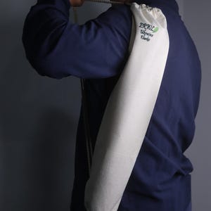 K&ouml;nnte beinhalten: Eine cremefarbene Yogamatten-Tasche mit Kordelzug, &uuml;ber der Schulter getragen. Auf der Tasche ist der Text "ERWL Ukraine Kharkiv" in Gr&uuml;n und Blau gestickt. Die Tasche ist zylindrisch und aus einem strukturierten Stoff.
