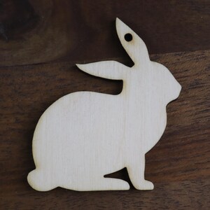 May include: A white wooden rabbit cutout, perfect for crafting and decorating. The rabbit is in a sitting position with its ears upright.