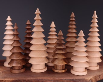 Op de afbeelding: Een set van acht houten kerstboompjes in verschillende maten, sommige geverfd in een lichtbruine kleur en andere in een natuurlijke houtkleur. De boompjes zijn gerangschikt op een houten oppervlak.