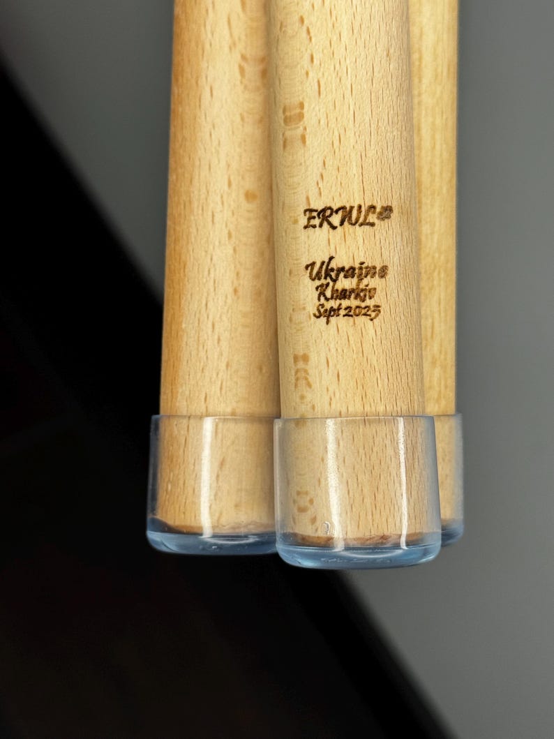 K&ouml;nnte beinhalten: Nahaufnahme von mehreren Holzd&uuml;beln mit transparenten Kunststoff-Endkappen. Der Text "ERWUL" und "Ukraine Kharkiv Sept 2023" ist in das Holz graviert. Die D&uuml;bel sind hellbraun.