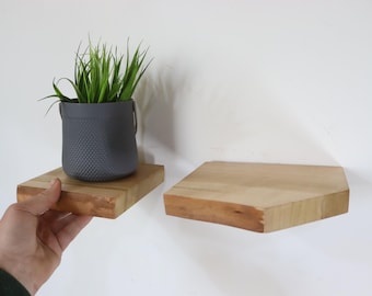 Op de afbeelding: Twee houten planken gemonteerd aan een witte muur. De plank links heeft een kleine plant in een pot met groene bladeren. De planken zijn gemaakt van licht hout en hebben een licht afgeschuinde rand.