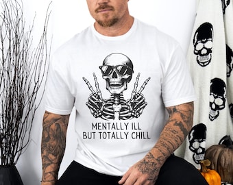 Puede incluir: Camiseta blanca con un esqueleto en blanco y negro con gafas de sol y haciendo el signo de la paz. El texto "MENTALLY ILL BUT TOTALLY CHILL" está impreso debajo. La camiseta es de estilo casual.