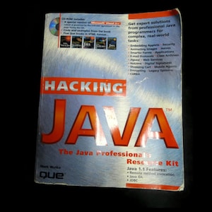 Peut inclure: Un livre intitulé "Hacking Java" avec des lettres orange et rouges sur un fond argenté. Le livre comprend un CD-ROM et propose des solutions pour les programmeurs Java. L'auteur est Mark Wutka, publié par Que.