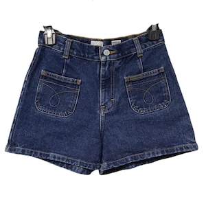 Peut inclure: Un short en jean bleu foncé avec de grandes poches plaquées sur le devant. Le short a une taille haute et une coupe ample.