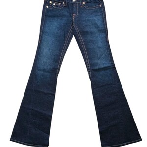 May include: Dark wash denim jeans with a flared leg. The jeans feature orange stitching, a button and zipper closure, and classic five-pocket styling. The back pockets have a signature design. The jeans are displayed on a white background.