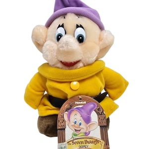 May include: A Dopey plush doll from Disney's The Seven Dwarfs, with a purple hat and yellow outfit. The doll has a tag featuring an illustration of Dopey and the text "The Seven Dwarfs Dopey".