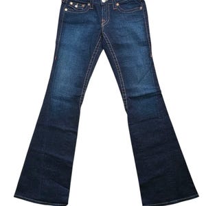 May include: Dark wash denim jeans with a flared leg. The jeans feature orange stitching, a button and zipper closure, and classic five-pocket styling. The back pockets have a signature design. The jeans are a classic style.