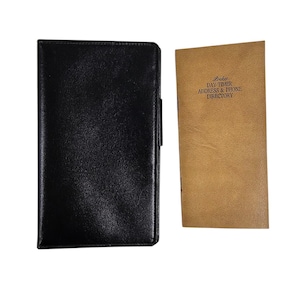 May include: A black leather-bound address book and a tan-colored Pocket Day-Timer Address & Phone Directory. The address book is closed, while the directory is open, displaying its printed text. Both items are rectangular.