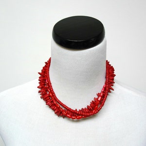 May include: A multi-strand necklace made of red wooden beads. The beads are in various shapes and sizes, creating a layered and textured look.