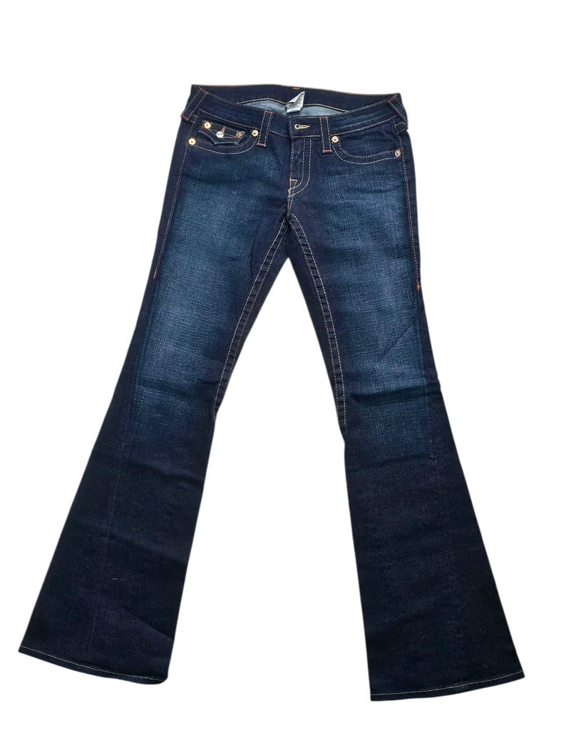 May include: Dark wash denim jeans with a flared leg. The jeans feature classic five-pocket styling, copper-colored stitching, and a button and zipper closure. The back pockets have a decorative stitch design.