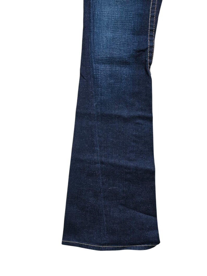 May include: Dark wash denim jeans with a flared leg. The jeans have white stitching along the seams and a classic five-pocket design. The fabric has a slight fade, giving it a worn look.