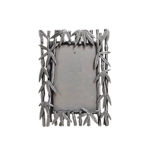May include: A rectangular silver-colored picture frame with a bamboo design. The frame features bamboo stalks and leaves around the edges, with a blank space in the center for a photo. The frame is made of metal.