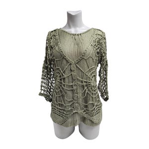 May include: Sage green crochet top with a V-neck and three-quarter sleeves. The top has a button-up front and a unique openwork design with circular patterns. The sleeves have a net-like pattern. The top is displayed on a white mannequin.