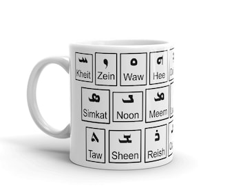 Puede incluir: Taza de cerámica blanca con letras árabes negras y palabras en inglés. Las letras están dispuestas en una cuadrícula. Las palabras son "Kheit", "Zein", "Waw", "Hee", "Simkat", "Noon", "Meem", "Taw", "Sheen" y "Reish".