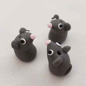 May include: Three small gray clay mice with black eyes and pink noses. The mice are standing on a white surface.