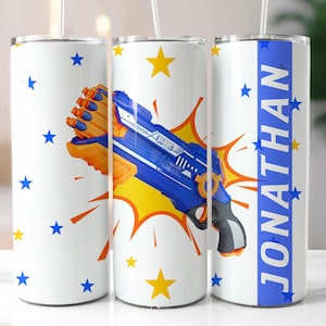 May include: Three white stainless steel tumblers with lids and straws. The centre tumbler features a blue and orange toy gun with a yellow starburst behind it. The tumbler on the right has a blue stripe with the name "JONATHAN" in white letters. The tumbler on the left has blue stars on a white background.
