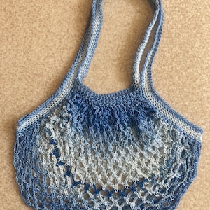 May include: A blue and white crocheted mesh bag with two long handles. The bag is made of a soft, lightweight material and has a gradient design.