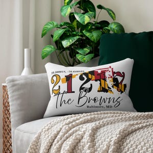 May include: White rectangular cushion featuring the text "21212 The Browns Baltimore, MD" in black script. The design includes a map outline and the Maryland state flag colours. Coordinates are printed above.