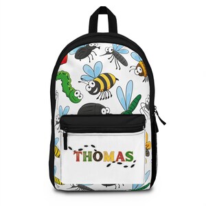 Op de afbeelding: Zwart-witte rugzak met een witte voorzak. De rugzak heeft een kleurrijk patroon van cartoon insecten, waaronder bijen, libellen en kevers. De naam "THOMAS" staat in kleurrijke letters op de voorzak.