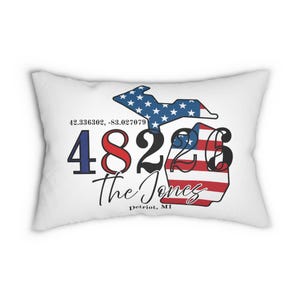May include: White rectangular cushion with a design featuring the state of Michigan in red, white, and blue, with the text "48226 The Jones Patriot, MI" and coordinates.