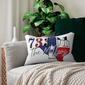 May include: White rectangular cushion featuring a Texas outline design. The design includes the text "73301 The Millers Austin, TX" in red, white, and blue. Coordinates are printed at the top. The cushion is on a grey sofa.
