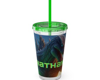 以下が含まれることがあります： 緑色の蓋とストローが付いた透明なプラスチック製のタンブラー。タンブラーには、緑色と青色の恐竜のグラフィックが描かれており、前面には「NATHAN」という名前が印刷されています。