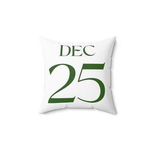 May include: White square cushion featuring the text "DEC 25" in dark green. This decorative cushion is a festive item, suitable for home or holiday decoration.