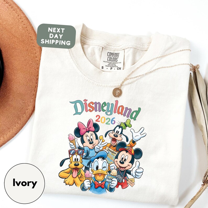 A white t-shirt with a colorful graphic of Disney characters from the theme park, along with a green shipping label and a beige hat.