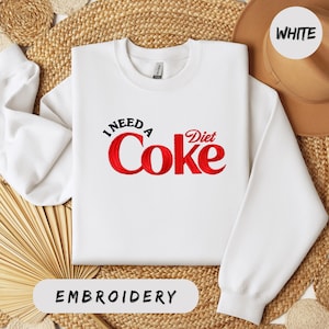 a white sweatshirt with a red Coca Cola logo, laid out on a woven straw mat.