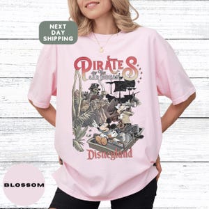 A woman wearing a pink t-shirt with a graphic of Disney characters and text related to the Pirates of the Caribbean ride at Disneyland.