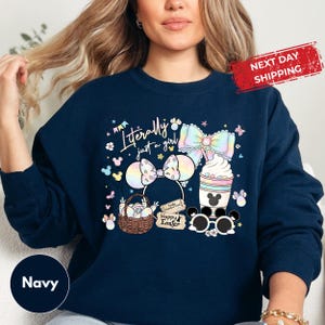 May include: Navy blue sweatshirt with a colorful graphic featuring a bow, Mickey Mouse ears, a basket of eggs, and a drink. The text "Literally just a girl" and "Happy Easter" are also displayed. A "Next Day Shipping" label is visible.