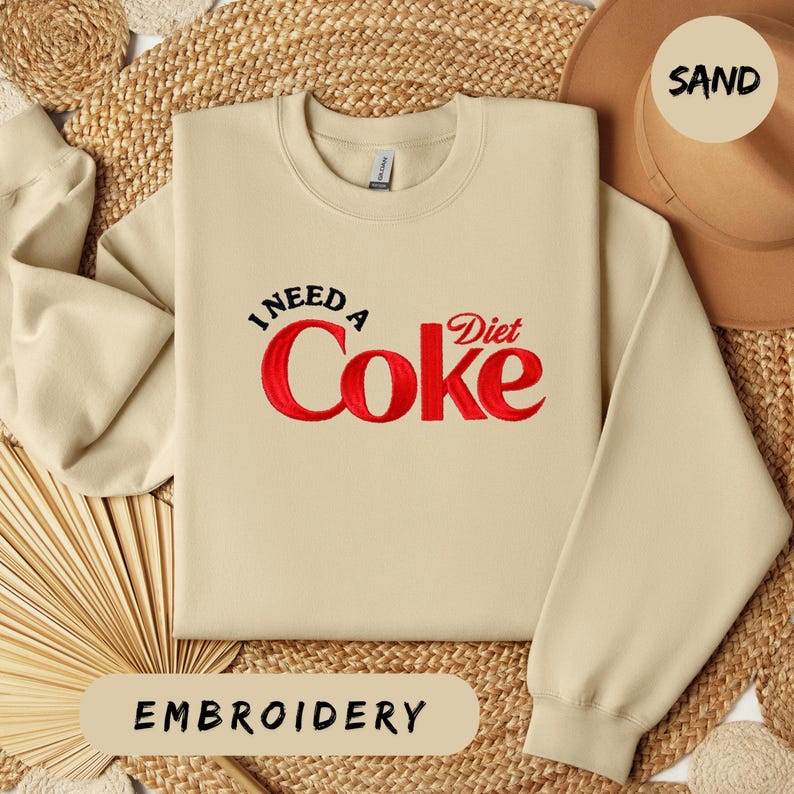 a beige sweater with a red Coca Cola logo, a straw hat, and a woven mat, all arranged on a straw mat.