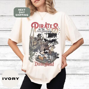 A woman wearing a white t-shirt with a graphic design of Disney's Pirates of the Caribbean on it.
