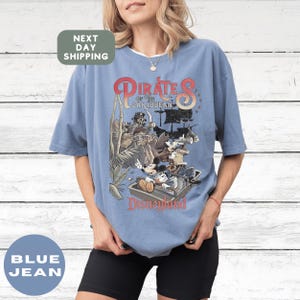 A woman wearing a blue t-shirt with a graphic of Disney characters and text related to the Pirates of the Caribbean ride at Disneyland.