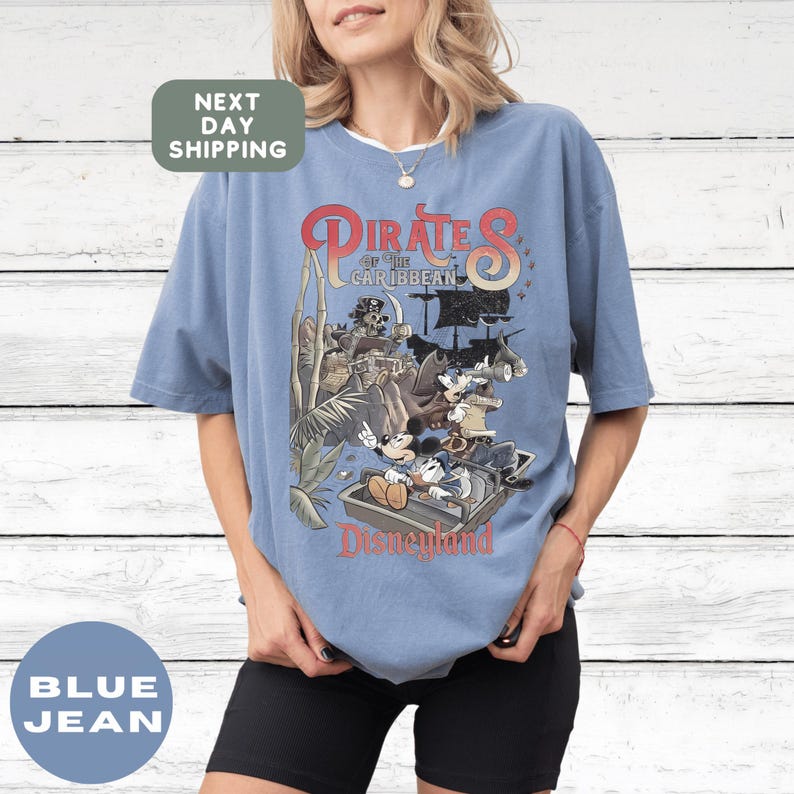 A woman wearing a blue t-shirt with a graphic of Disney characters and text related to the Pirates of the Caribbean ride at Disneyland.