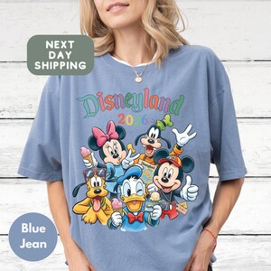 A woman wearing a blue t-shirt with a colorful graphic of Disney characters from the theme park.