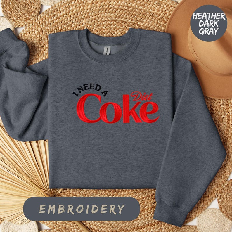 a gray sweatshirt with a red Coca Cola logo, laid out on a woven mat.