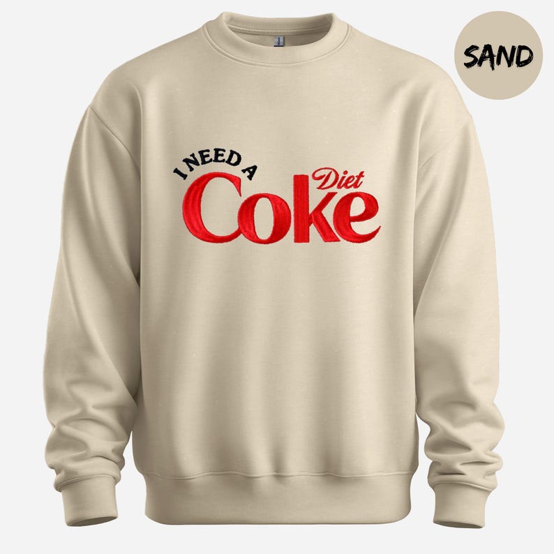A beige sweatshirt with a red and black text design that says "I NEED A Diet Coke".