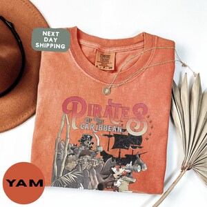 a red t-shirt with a pirate-themed graphic, a hat, and a necklace, all placed on a white background.