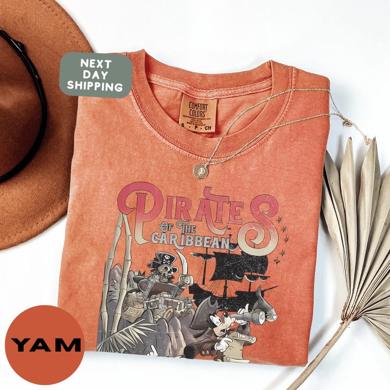 a red t-shirt with a pirate-themed graphic, a hat, and a necklace, all placed on a white background.