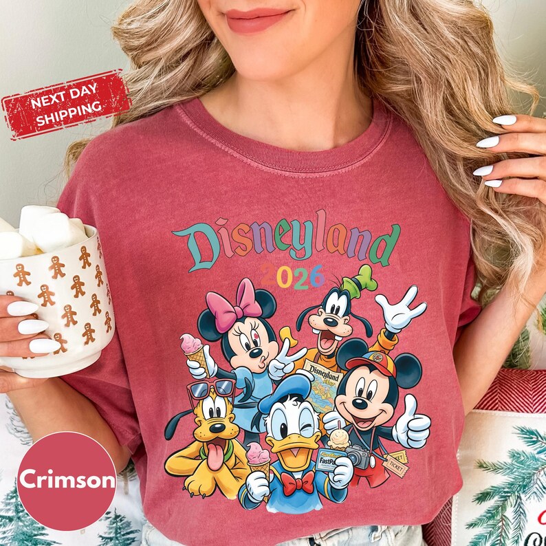 A woman wearing a red t-shirt with a Disneyland graphic and holding a mug of marshmallows.