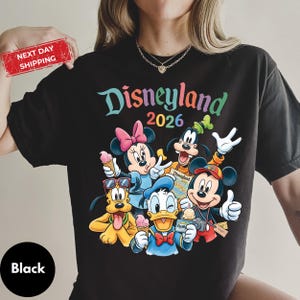A person wearing a black t-shirt with a colorful graphic of Disney characters and text.